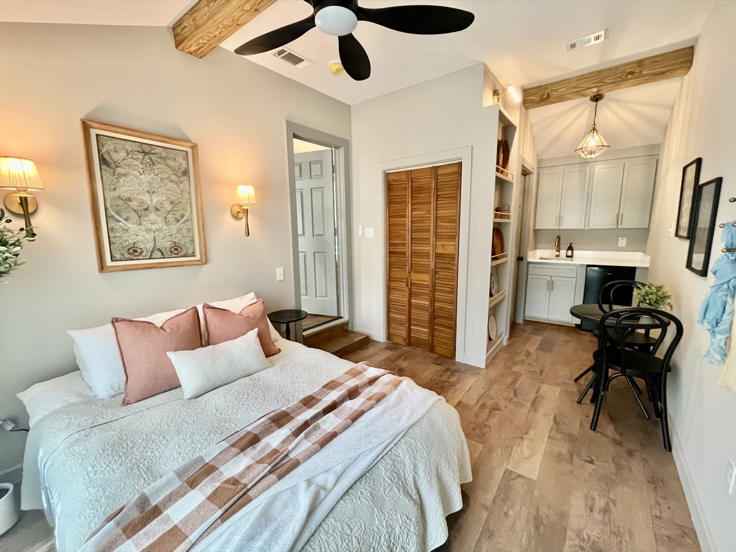 Staged bedroom with exposed wood beams, ceiling fan, and kitchenette